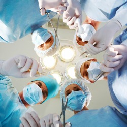 Below view of surgeons holding medical instruments in hands and looking at patient