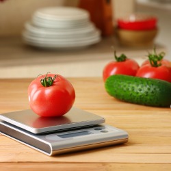 Fresh tomato with digital kitchen scales on wooden table