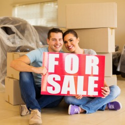 moving couple holding for sale sign at home