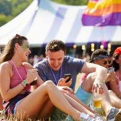 Friends sitting on grass using smartphone at music festival