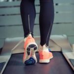 Fitness girl with muscular legs running on treadmill in the gym