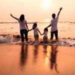 Happy family holding hands on beach and watching the sunset