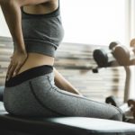 Young woman having back pain after workout at the gym.