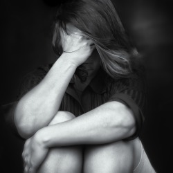 Black and white image of a young woman crying and covering her face useful to illustrate stress, depression or domestic violence