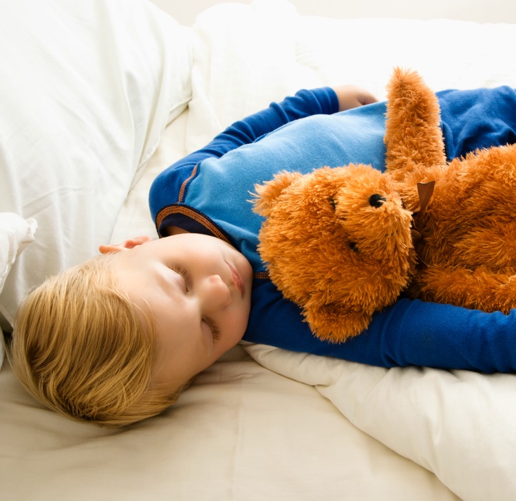Caucasian toddler boy sleeping in bed with teddy bear.