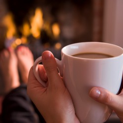 Feet warming at a fireplace with hands holding coffee