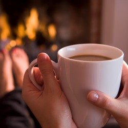 Feet warming at a fireplace with hands holding coffee