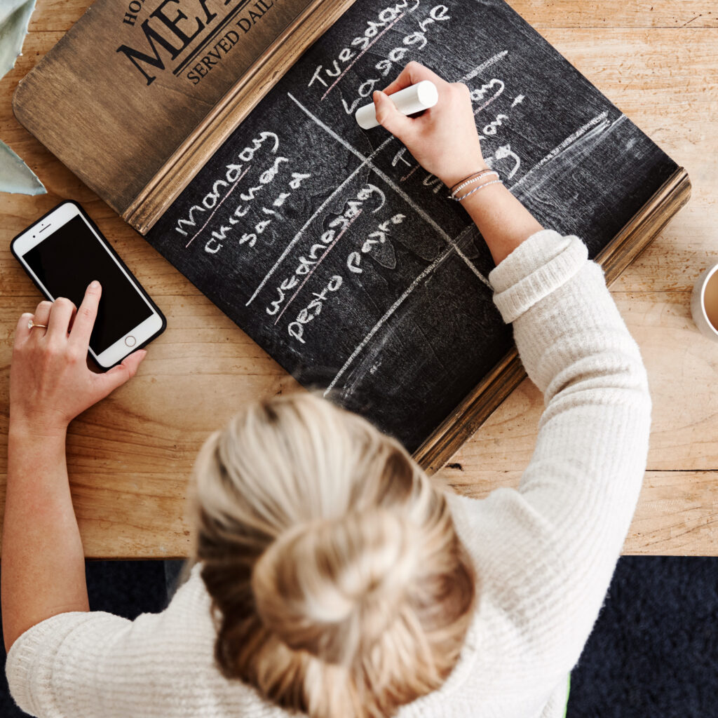 Overhead Shot Looking Down On Woman At Home Writing Meal Plan