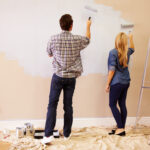 Couple Decorating Room Using Paint Rollers On Wall