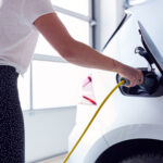Close Up Of Woman Charging Electric Vehicle With Cable In Garage At Home